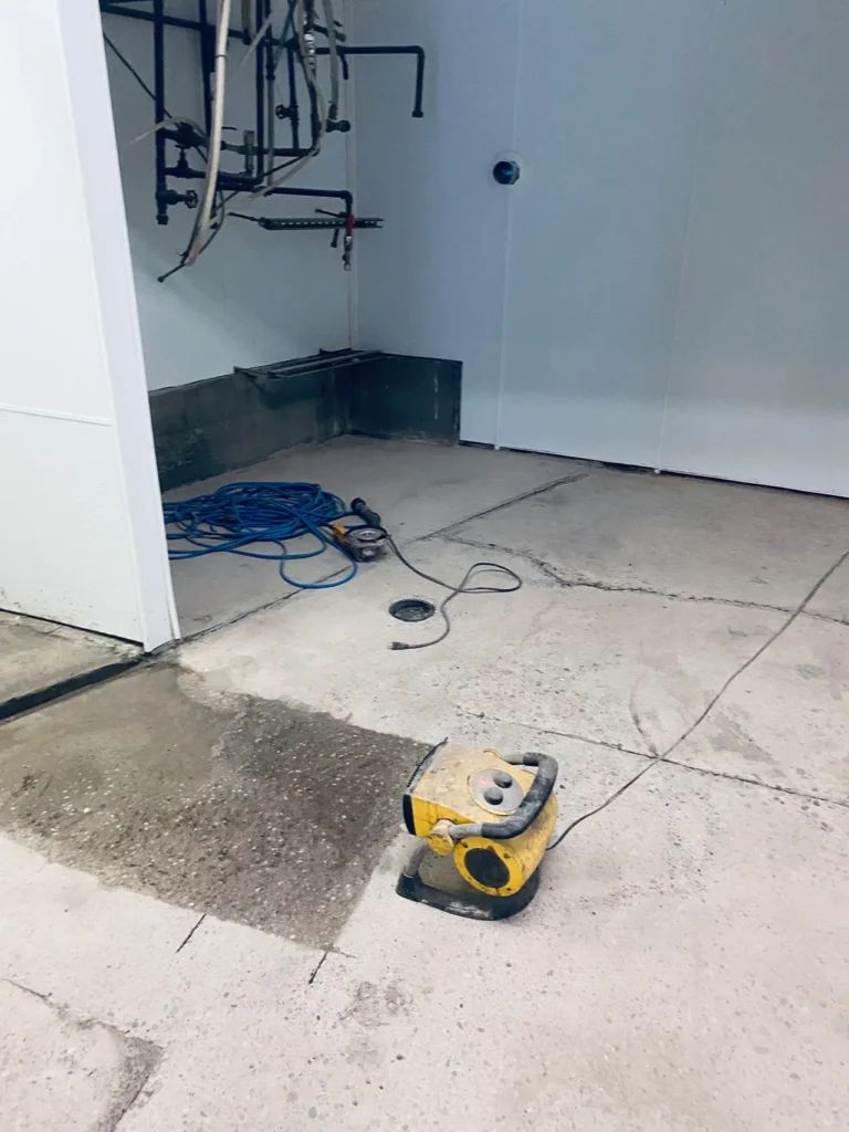 Construction site with tools, including a cement cutter and electrical cables, organized along a wall in a room with bare floors.